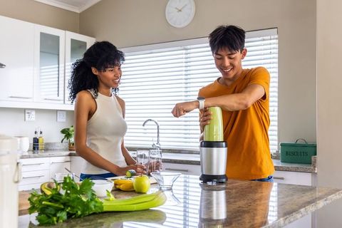 Young diverse couple making green smoothie on bright modern kitchen island