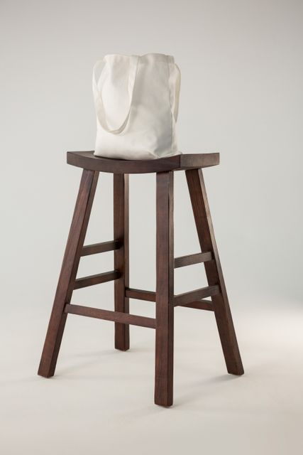 White bag placed on wooden stool against white background. Ideal for use in minimalist design concepts, interior decor ideas, product display, fashion accessory promotions, and modern home decor inspiration.