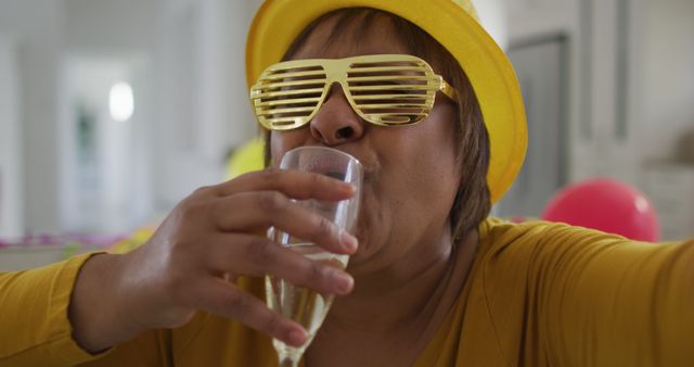 Woman in yellow hat wearing shutter sunglasses enjoying a casual celebration. Suitable for depicting festive events, social gatherings, parties, or lifestyle content focusing on joyous moments. Perfect for advertising party supplies, celebration themes, and social event promotions.