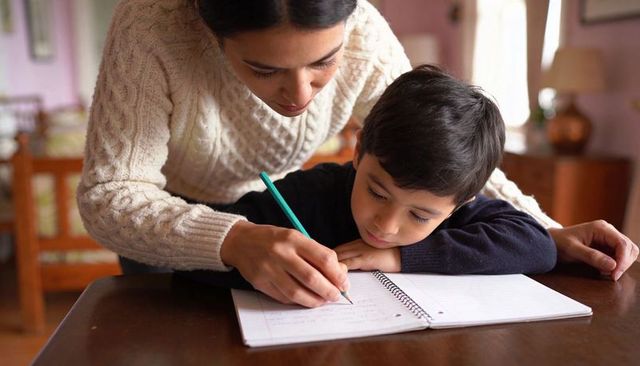 Mother helping son practice handwriting at home, cozy homeschool learning moment
