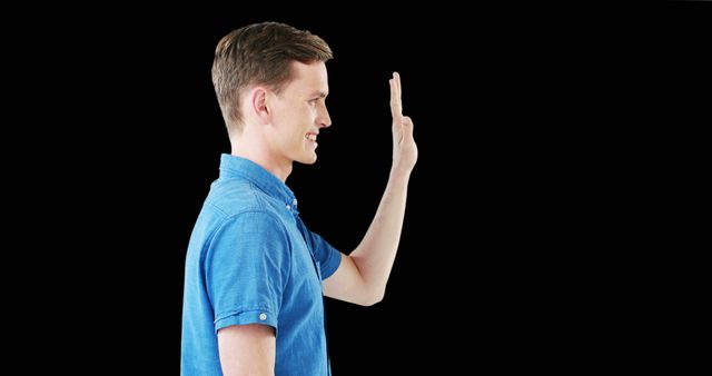 Man in blue shirt waving with smile; black background enhances focus on individual. Perfect for concepts of greeting, introduction, friendly interaction, and welcoming messages. Ideal for websites, advertisements, or communication materials.