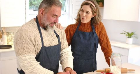 Couple kneading dough at home kitchen island wearing denim aprons cozy bright lifestyle