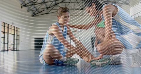 Female basketball teammates tying shoes and stretching on indoor court with wave overlay