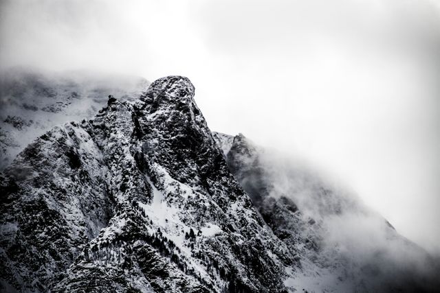 Snow-covered mountain peak shrouded in mist creates a dramatic and rugged scene. Ideal for use in winter travel advertising, extreme sports promotions, or landscape photography inspiration. This natural landscape captures the near awe-inspiring beauty and harsh conditions of high-altitude environments.