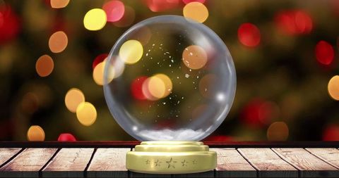 Glass snow globe with golden base and festive bokeh lights