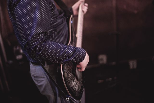Man is playing electric guitar in a low light environment, evoking a live music performance atmosphere. Perfect for use in articles about live music, performance art, night gigs, and musician profiles. Ideal for promoting music events or lessons.