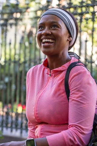 Smiling african american woman wearing headband and pink jacket looking up outdoors