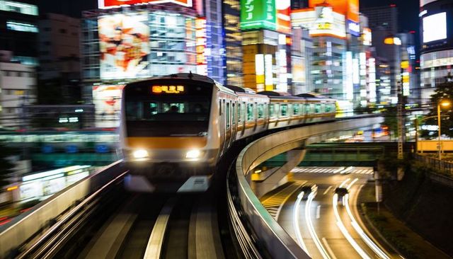 Racing commuter train rounding elevated curve through neon-lit city night, motion blur