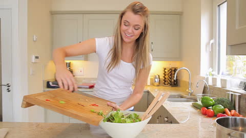 Smiling Woman Preparing Fresh Salad in Bright Kitchen