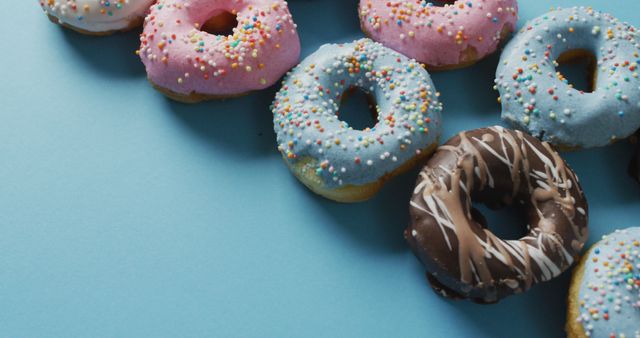 Collection of colorful donuts with various toppings on blue background, ideal for use in marketing materials related to bakeries, sweets, and dessert shops. Can be utilized in blog posts, social media graphics, or as a visual element in menu designs.