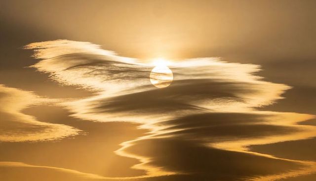 Dramatic golden sunrise casting radiant light through layered cirrus clouds over open sky
