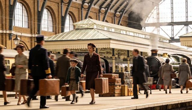 Mother and son walking hand-in-hand on bustling 1940s train platform with steam locomotive