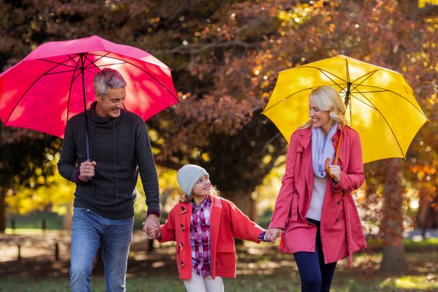 Cheerful parents with daughter walking at park while holding umbrella at park