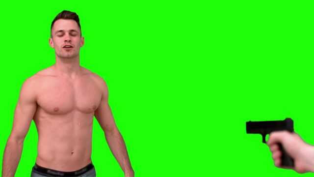 Shirtless man standing with eyes closed while a gun is pointed at him on a green screen background. This dynamic and tense scene is perfect for use in visual effects, film and television production, or media projects that require the addition of dramatic and dangerous action elements.