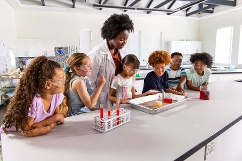 Teacher guiding diverse elementary students during hands-on classroom chemistry experiment