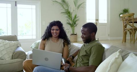 Couple reacting to notification while browsing laptop and phone on cozy living room sofa