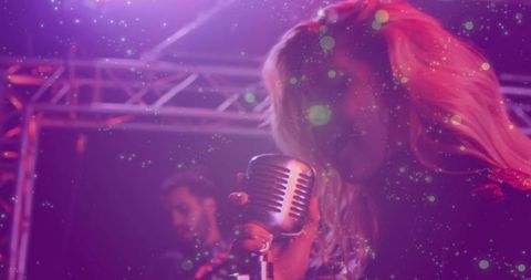 Blonde vocalist singing into vintage chrome microphone on neon purple stage with band