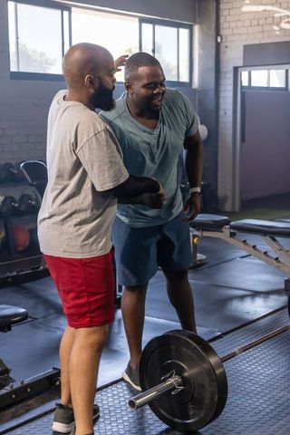 Two men spotting barbell deadlift showing teamwork, motivation and gym camaraderie