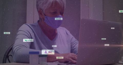 Senior woman wearing mask typing on laptop logging medications with digital health alerts