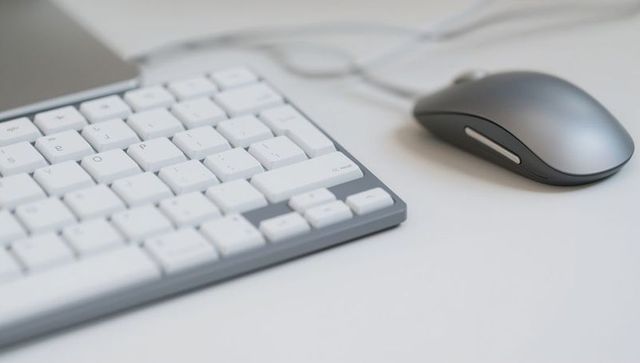 Minimalist desk workspace featuring compact white keyboard and silver wired mouse