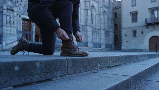 Kneeling man tying scuffed leather boots on cathedral stone steps urban travel lifestyle