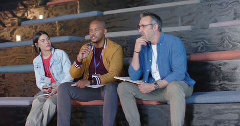 Panelists discussing ideas on auditorium steps with microphone and notebooks, wearing lanyards