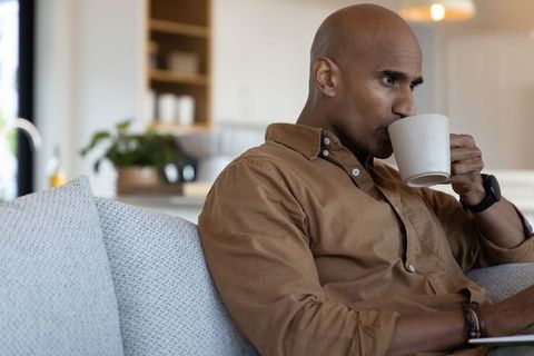African american man sipping coffee on sofa in modern open-plan kitchen, cozy lifestyle