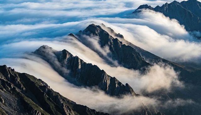 Jagged Alpine Ridge Cutting Through Rolling Fog Over High Mountain Peaks at Sunrise