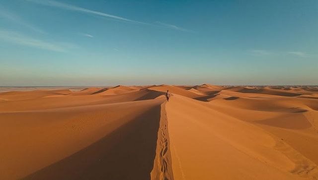 Walking hiker along sand dune ridge leaving footprints across expansive desert horizon