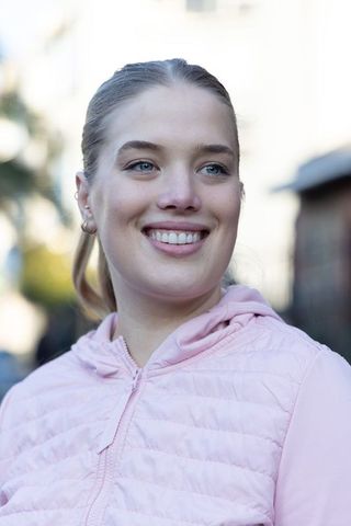 Smiling young woman wearing pink quilted hooded jacket strolling urban street
