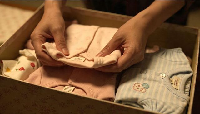 Hands folding baby onesies in floral box newborn wardrobe organization
