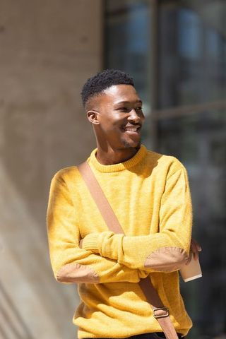 African american man smiling holding coffee wearing mustard sweater crossbody bag urban portrait