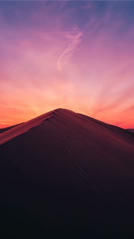 Vertical camera moving along dune ridge at twilight capturing vivid desert sunset colors