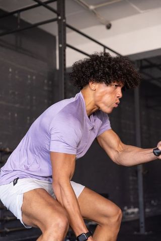 African american man performing bent-over cable row in gym wearing smartwatch and shorts