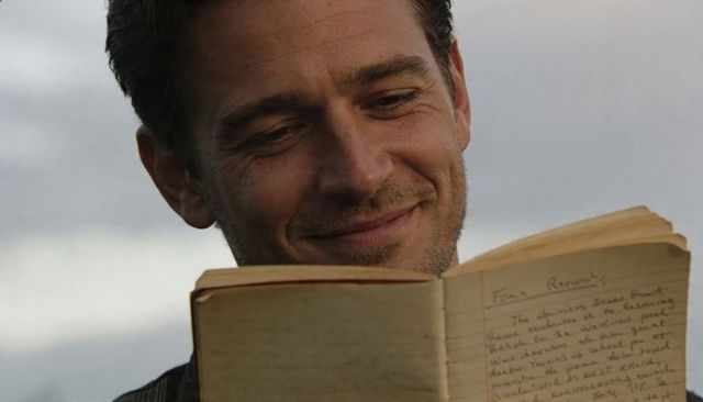 Smiling man reading weathered journal outdoors at golden hour, closeup of handwritten pages