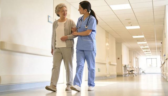 Nurse helping senior woman walking down hospital corridor, compassionate care