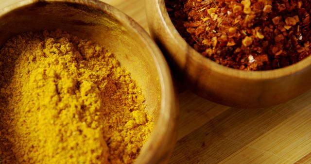 Ground turmeric and crushed red pepper flakes are presented in wooden bowls, showcasing a variety of spices used in culinary dishes. Their vibrant colors and textures highlight the diversity and importance of spices in enhancing flavor and aroma in cooking.