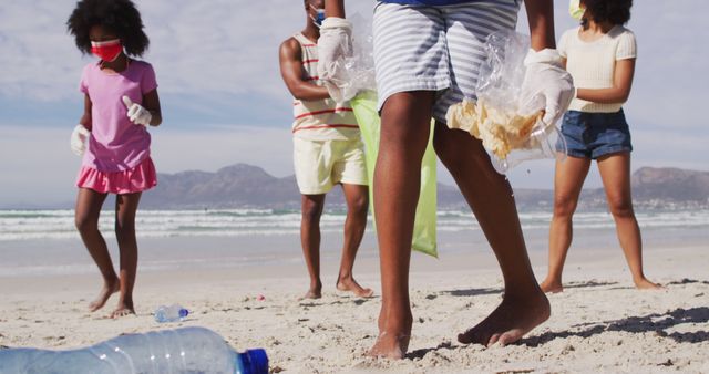 African american parents with two children wearing face masks collecting rubbish from the beach. family eco beach conservation during covid 19 coronavirus pandemic.