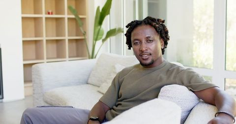 Relaxed man lounging on modern sofa in bright minimalist living room with plants