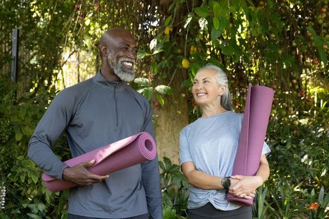 Active mature couple carrying purple yoga mats in sunlit garden for outdoor fitness