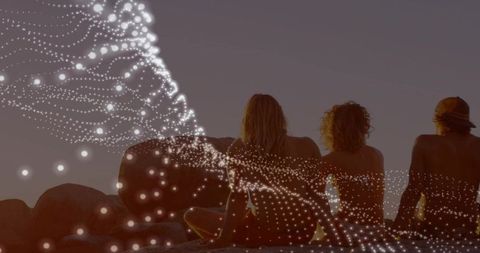 Four friends sitting on coastal boulders watching sunset with digital particle overlay