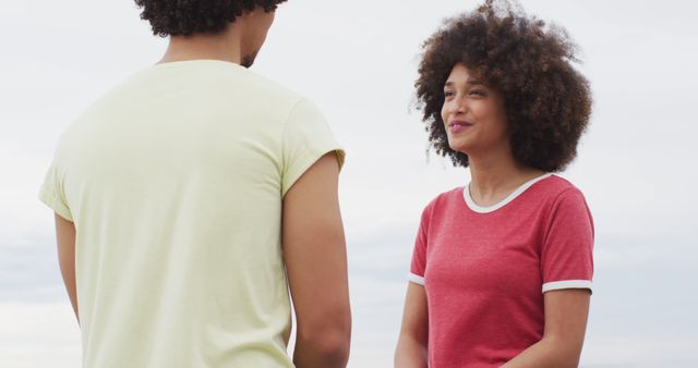 Young couple engaging in friendly conversation outdoors on a summer day, wearing casual clothes with afro hair. Ideal for use in content related to friendships, relationships, youth, and lifestyle themes. Suitable for social media campaigns, blog posts, and advertisements emphasizing connection and casual interactions.