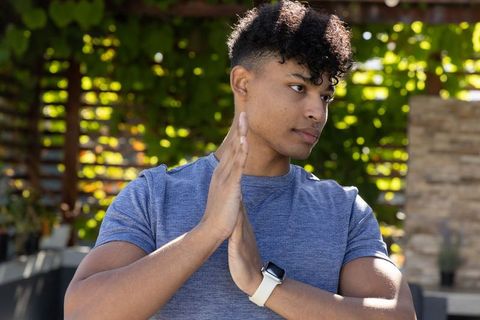 African american man posing on sunlit patio pressing hands together wearing smartwatch