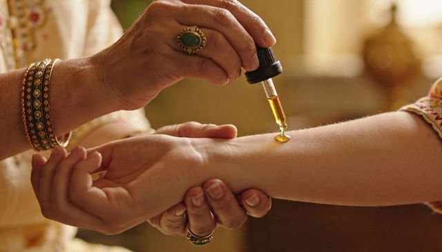 Applying golden ritual oil with dropper on forearm, intimate traditional self-care
