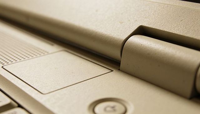 Beige laptop hinge and palm rest close-up with touchpad, power button, textured plastic
