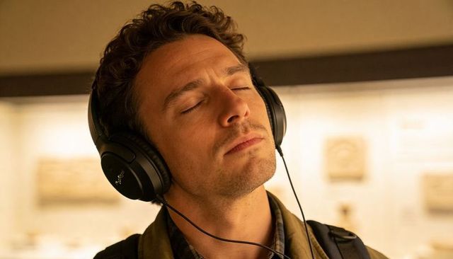 Man listening with over-ear headphones and closed eyes in museum gallery