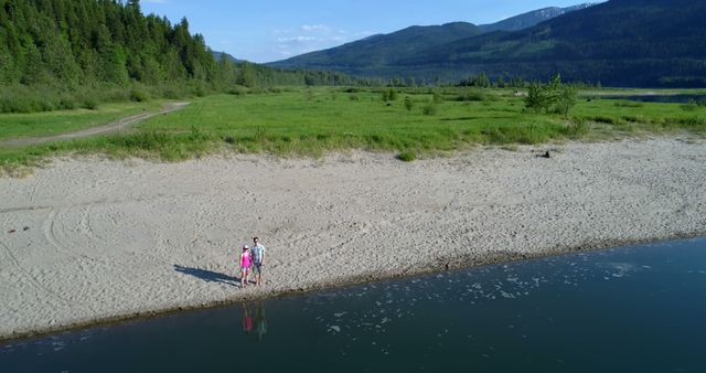 Couple Standing on Serene Sandy Beach Near Forest and Mountain Range - Download Free Stock Images Pikwizard.com