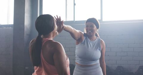 Women high-fiving after strength training in gym smiling workout partners in athleisure