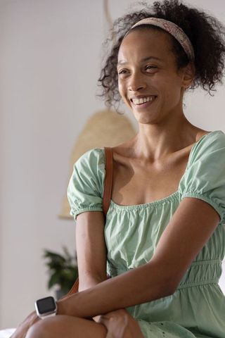 Smiling woman wearing green dress, headband and smartwatch sitting in modern living room
