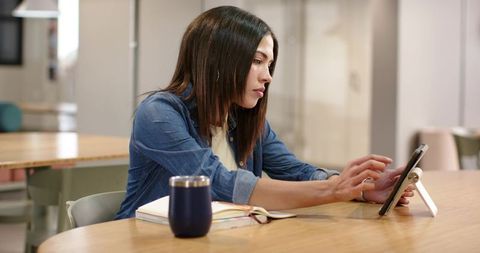 African american woman working on tablet at modern coworking table in denim shirt, focused